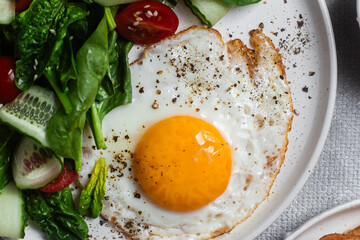 Fried egg with spinach, tomato and cucumber salad in a white plate. Healthy breakfast