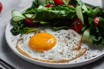 Fried egg with spinach, tomato and cucumber salad in a white plate. Healthy breakfast