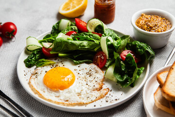 Fried egg with spinach, tomato and cucumber salad in a white plate. Healthy breakfast