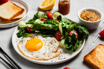 Fried egg with spinach, tomato and cucumber salad in a white plate. Healthy breakfast