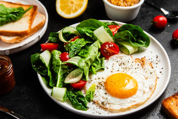 Fried egg with spinach, tomato and cucumber salad in a white plate. Healthy breakfast