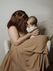 Mère avec son bébé dans les bras sur un fauteuil blanc en studio