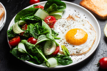 Fried egg with spinach, tomato and cucumber salad in a white plate. Healthy breakfast