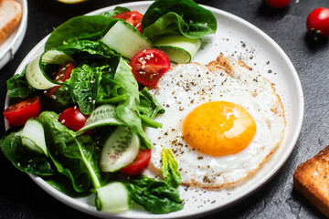 Fried egg with spinach, tomato and cucumber salad in a white plate. Healthy breakfast