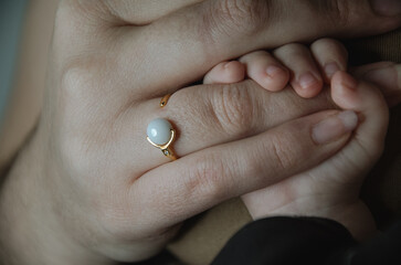 Bébé tenant la main de sa mère qui porte une bague avec une perle blanche