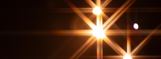 Multiple bright stage lights form vivid starburst patterns against a dark background, creating an...