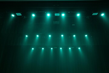 A dimly lit stage bathed in green lighting, with sheets of paper scattered across the floor....