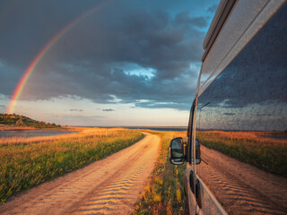 view to rainbow and ground road between glass of commercial van under dramatic sky