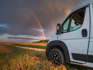landscape view to head of white commercial van and rainbow in sky with copy space