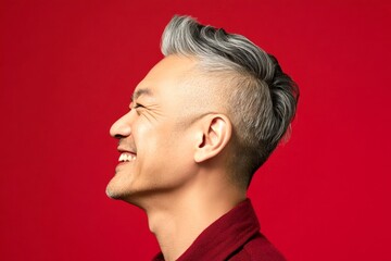 Fototapeta premium Red solid background. A modern and happy gentleman enjoying his moment. Modish men's disconnected undercut haircut - midlife asian man with short hair. Creative of style for aging men.