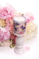Decorative natural flower candle on a stand and on the background of a pink and white bouquet. Isolate on a white background