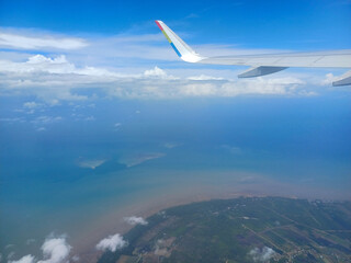Obraz premium From an airplane window, a view of Indonesia unfolds. Islands are scattered across the turquoise sea, with a patchwork of green rice paddies and coastal villages visible below, provides perspective