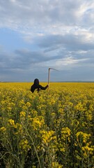 A person dressed in black walking through a rapeseed field, holding a scythe