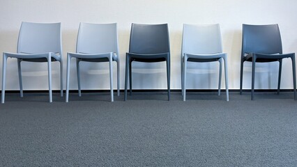 A row of modern chairs in front of a white wall in a minimalist interior. Empty waiting room at a...