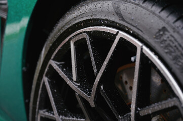 close-up of wet car tire and alloy wheel on sleek green vehicle showcasing modern automotive...