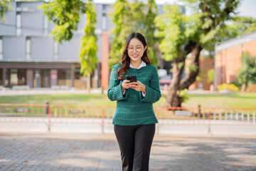 Fototapeta premium A female student walks through a university building with a notebook, earphones, smartphone, and is listening to music.