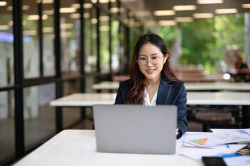 Asian businesswoman in suit using mobile phone while standing in front of modern business building.