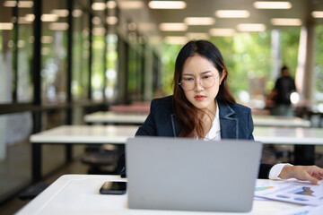 Asian businesswoman working on financial market research using laptop and digital tablet, stressed...