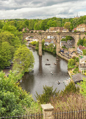 A historic stone viaduct crosses a river with boats.