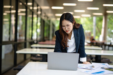 Obraz premium Asian businesswoman working on financial market research using laptop and digital tablet, stressed about digital investment in office.
