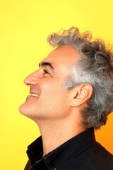 Fototapeta premium A midlife gentleman with grace and sophistication. Yellow solid background. Trendy men's wavy fringe haircut - midlife middle eastern man with middle hair. Creative of style for aging men.