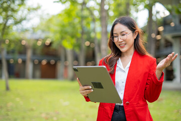 Fototapeta premium Asian businesswoman standing in front of modern business building and using tablet to work.