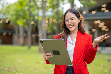 Fototapeta premium Asian businesswoman standing in front of modern business building and using tablet to work.