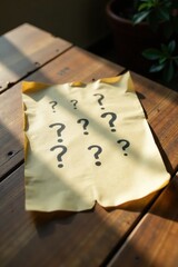 Unveiling a Mystery A Tan Paper with Multiple Question Marks Resting on a Wooden Table in Sunlight
