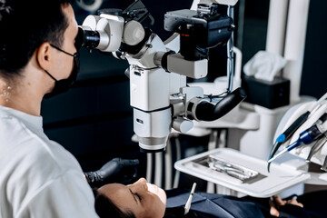 Dentist examining teeth condition using a surgical digital microscope in a dental clinic. Concept surgical microscope, dental diagnostics, precision treatment, oral examination.