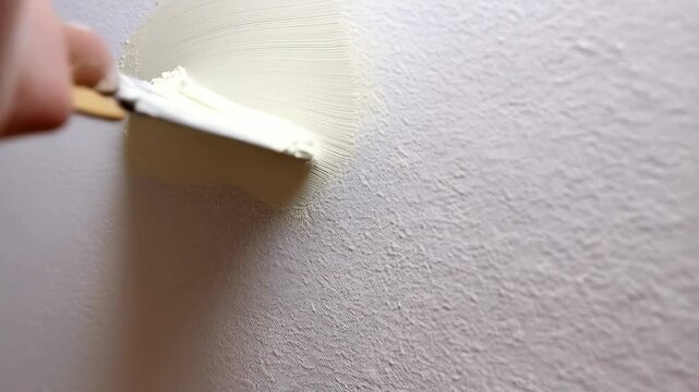 Hand applying putty with a spatula onto a textured wall to repair damage and improve its appearance for painting