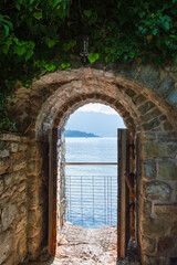 Fototapeta premium Stone entrance in the fortress wall with wooden doors overlooking the sea and mountains, frontal view