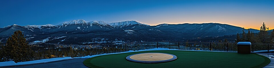 Luxurious Rooftop Helipad: Illuminated Circular Landing Zone with Glass Railings at Blue Hour. Aerial View of Exclusive Hotel Amenity Overlooking Golf Course and Snow-Capped Mountains