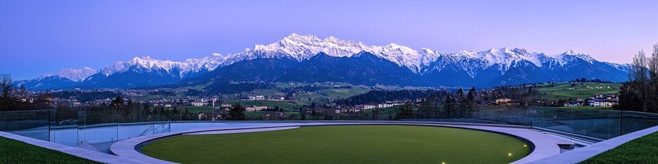 Luxurious Rooftop Helipad: Illuminated Circular Landing Zone with Glass Railings at Blue Hour. Aerial View of Exclusive Hotel Amenity Overlooking Golf Course and Snow-Capped Mountains