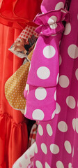 A close-up of colorful garments on a clothing rack features a pink polka-dot sleeve with ruffles,...
