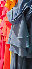 Colorful dresses with layered ruffles hang in a row, showcasing vibrant shades of blue, red,...