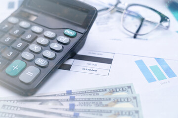 A calculator, financial charts, cash, and glasses on a desk, representing business calculations and financial analysis.