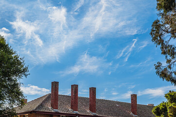 Old red brick chimneys sticking out of tile roof against blue sky background, Victoria, Australia