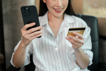 A woman in a striped shirt uses her smartphone and credit card for online shopping, sitting in a modern home office.