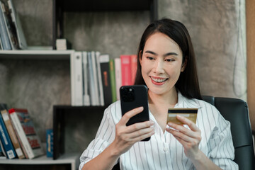 Fototapeta premium A woman happily uses her smartphone and credit card for online shopping in a stylish home office environment.