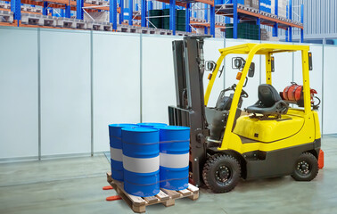 Yellow forklift handling blue industrial barrels on pallet inside warehouse with shelving in...