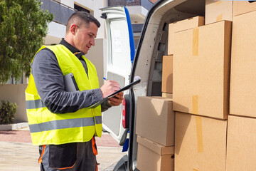 Delivery man near minivan. Parcels in trunk of postman car. Man courier takes notes. Delivery...
