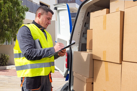 Delivery man near minivan. Parcels in trunk of postman car. Man courier takes notes. Delivery specialist. Courier delivered parcels to customer house. Delivery worker career. Parcel logistics