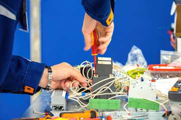 Electrician working with wires and circuit breakers on control panel, using screwdriver to install...