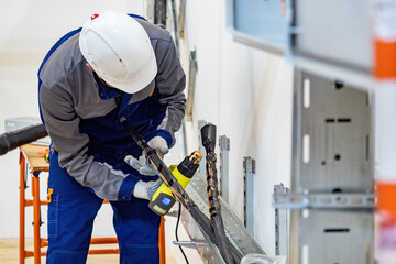 Electrician in hard hat uses heat gun to install heat shrink tubing on high-voltage cables in metal...
