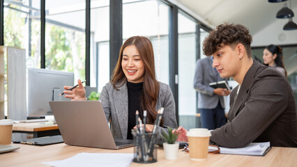 Confident businesswoman giving a presentation to her coworker using a laptop in a modern office.