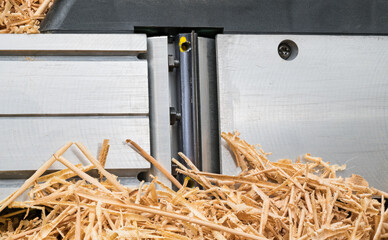 Long wooden swarf on metal plane detail with aluminum sole and sharp steel blade. Closeup a pile of thin rolled up wood shavings on planing tool with iron. Chip machining waste product at woodworking.