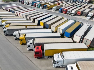 Gordijnen Aerial view of a large truck parking lot at a logistics hub, with multiple commercial semi trucks parked in organized rows © scharfsinn86