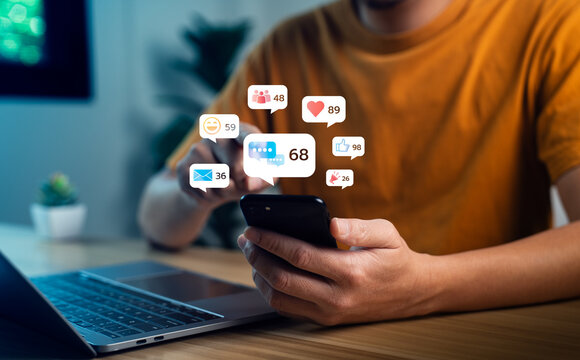 Close up of man using smartphone with social media notification icons such as like, heart, message, group, and email floating above screen, concept of digital communication and online engagement