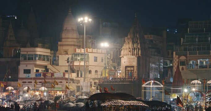Varanasi, Uttar Pradesh, India. Many people visiting Ganga Maha Aarti ceremony on Dashashwamedh Ghat. night time illumination lights. Cinematic Camera movement moving along riverbank embankment. View