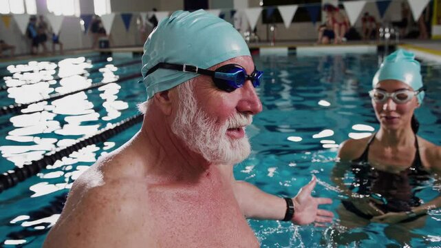Professional female instructor guiding mature swimmer during personalized aquatic training session in indoor swimming pool, focusing on technique improvement